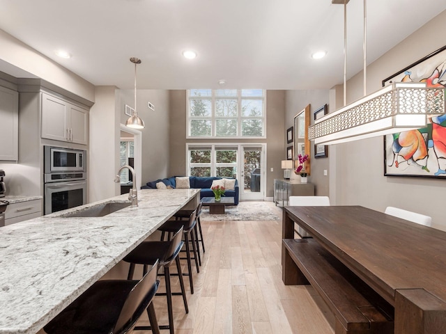 kitchen featuring appliances with stainless steel finishes, light stone countertops, gray cabinetry, light wood-style floors, and a sink