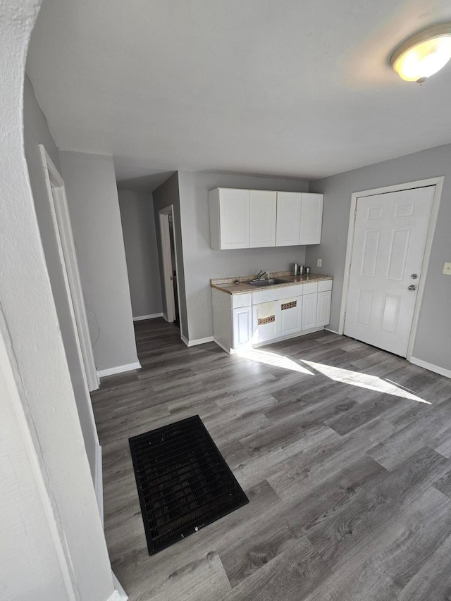 kitchen with wood finished floors, baseboards, a sink, light countertops, and white cabinets