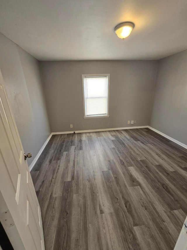 spare room with baseboards and dark wood-style flooring