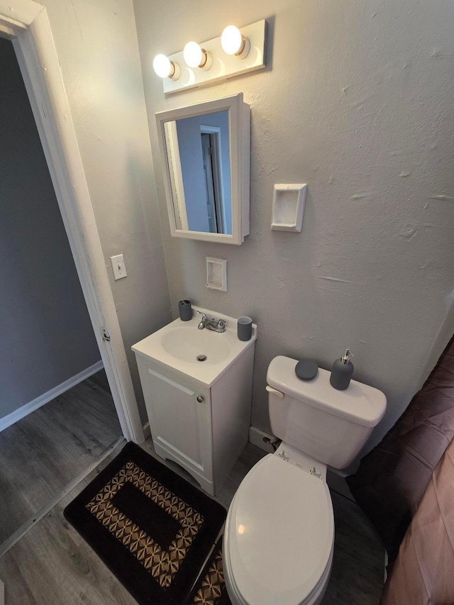 half bathroom featuring vanity, toilet, wood finished floors, and baseboards