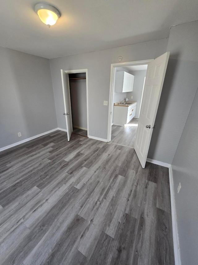 unfurnished bedroom with a closet, a sink, baseboards, and wood finished floors