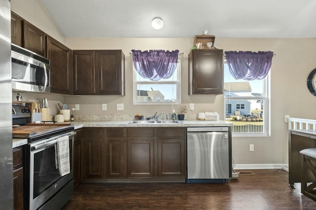 kitchen with dark brown cabinets, baseboards, appliances with stainless steel finishes, dark wood-style floors, and a sink