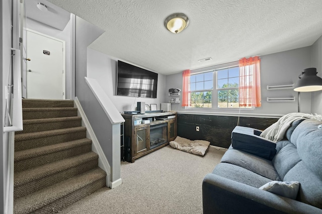 living area featuring carpet flooring, a textured ceiling, visible vents, and a wainscoted wall