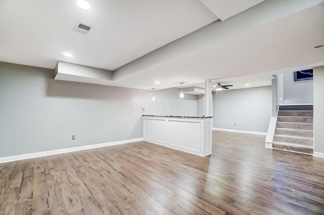 finished below grade area with baseboards, visible vents, stairway, and wood finished floors