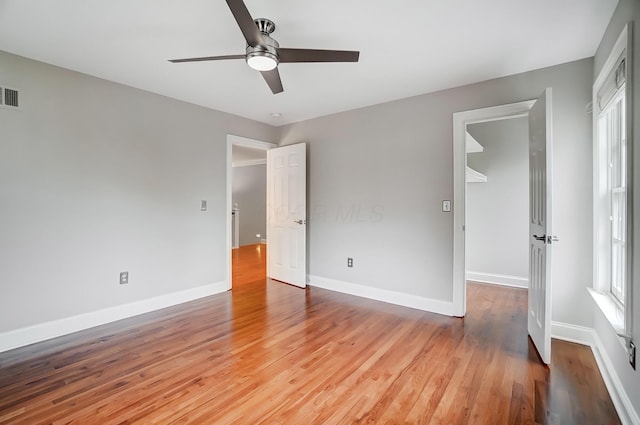 unfurnished bedroom with visible vents, baseboards, a walk in closet, and wood finished floors