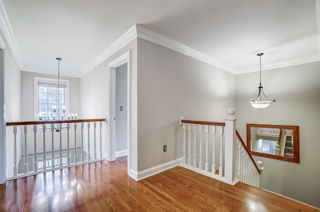 hall featuring baseboards, ornamental molding, wood finished floors, an upstairs landing, and a chandelier