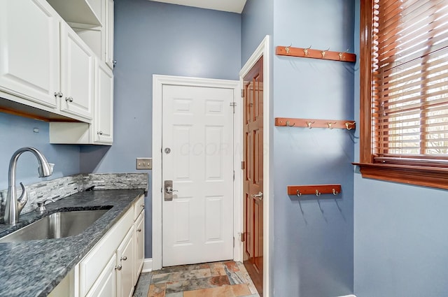 kitchen with stone finish floor, dark stone countertops, a sink, and white cabinetry