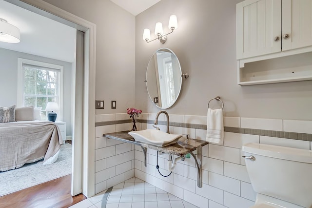 bathroom with ensuite bathroom, toilet, a sink, tile walls, and wainscoting