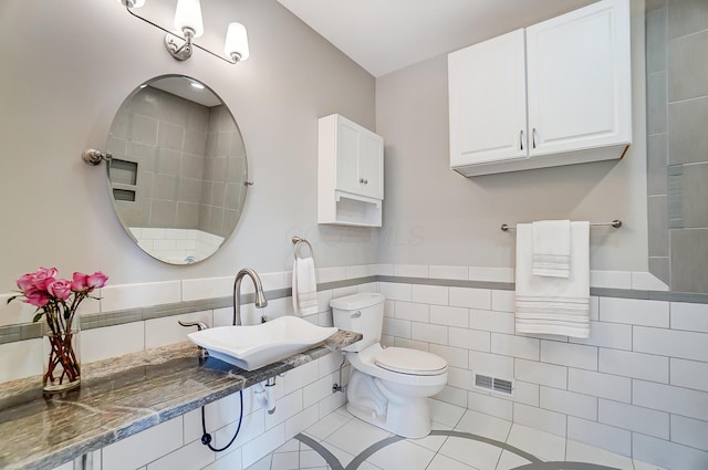 bathroom with a wainscoted wall, tile walls, toilet, a sink, and tile patterned flooring