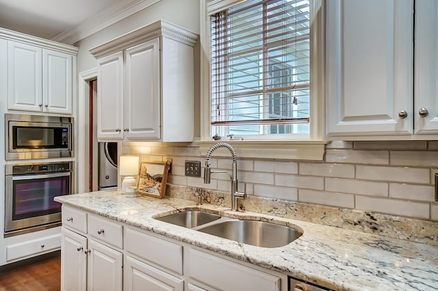 kitchen with tasteful backsplash, white cabinets, light stone counters, stainless steel appliances, and a sink