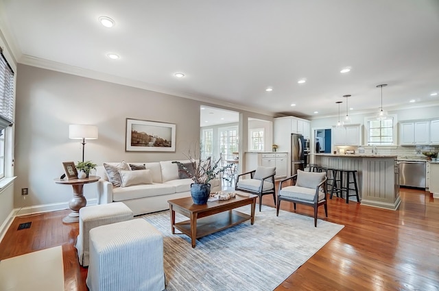 living room with baseboards, plenty of natural light, wood finished floors, and crown molding