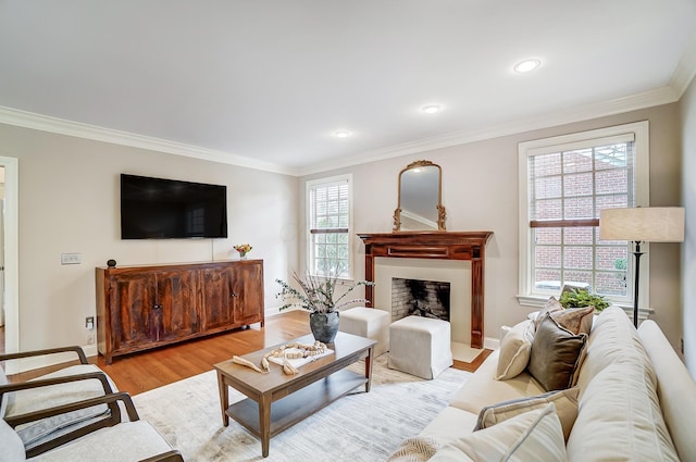 living area with a fireplace with raised hearth, baseboards, light wood-style flooring, and crown molding