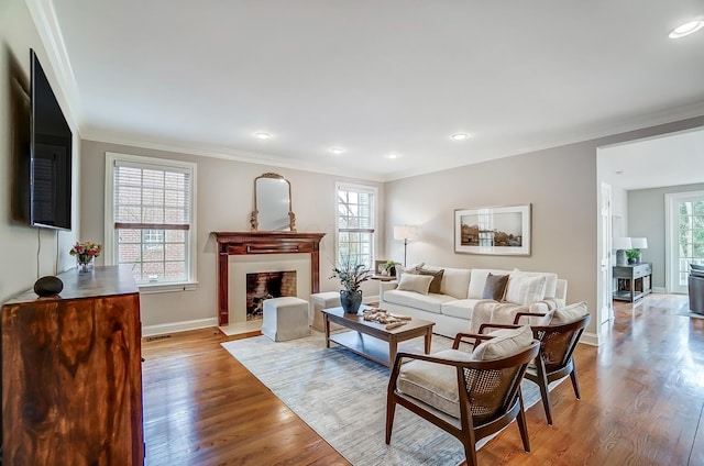 living area with ornamental molding, a fireplace, baseboards, and wood finished floors