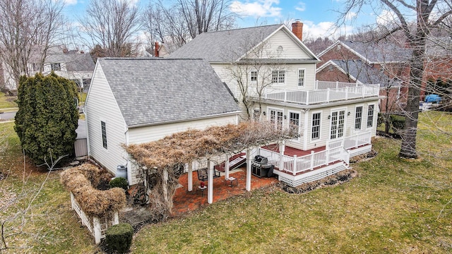 back of property featuring a lawn, a balcony, a chimney, roof with shingles, and a wooden deck