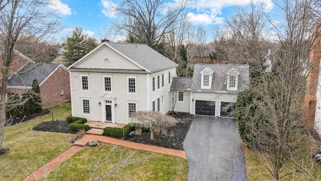 neoclassical / greek revival house featuring a garage, a shingled roof, a chimney, aphalt driveway, and a front lawn