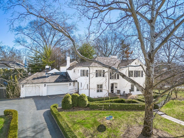 view of front of home with a garage, driveway, a chimney, and stucco siding