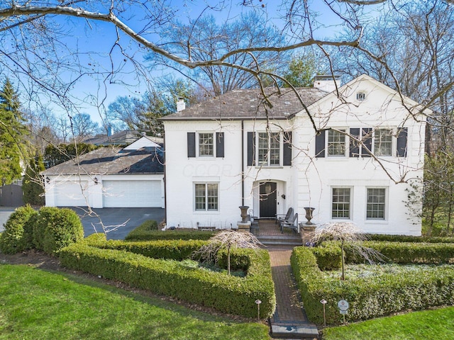 colonial house featuring aphalt driveway, a garage, and a chimney