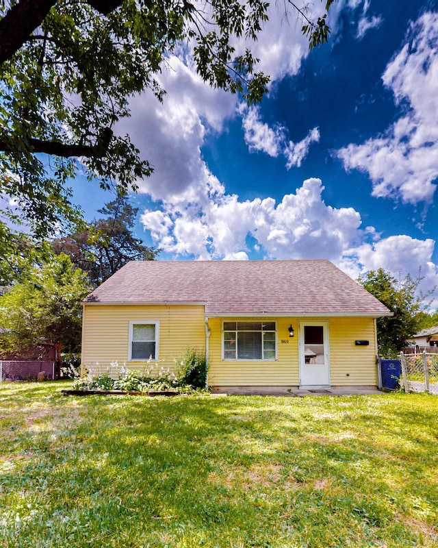 single story home featuring roof with shingles, a front yard, and fence