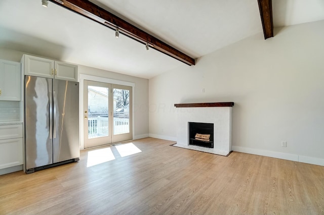 unfurnished living room featuring light wood-type flooring, a fireplace with flush hearth, track lighting, lofted ceiling with beams, and baseboards