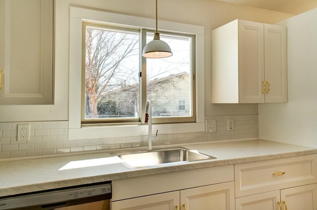 kitchen with a sink, hanging light fixtures, light countertops, dishwasher, and backsplash