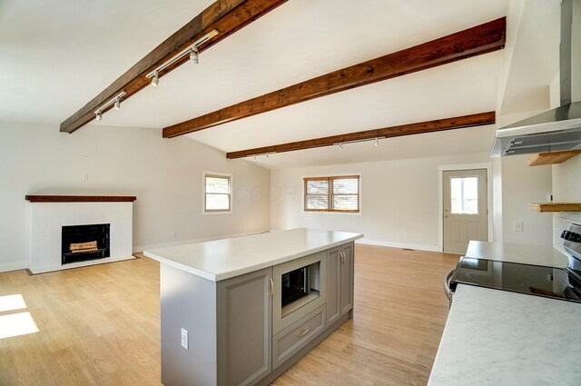 kitchen featuring open floor plan, gray cabinets, a fireplace with flush hearth, and wall chimney range hood