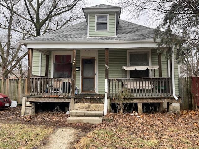 view of front of home featuring covered porch, a shingled roof, and fence