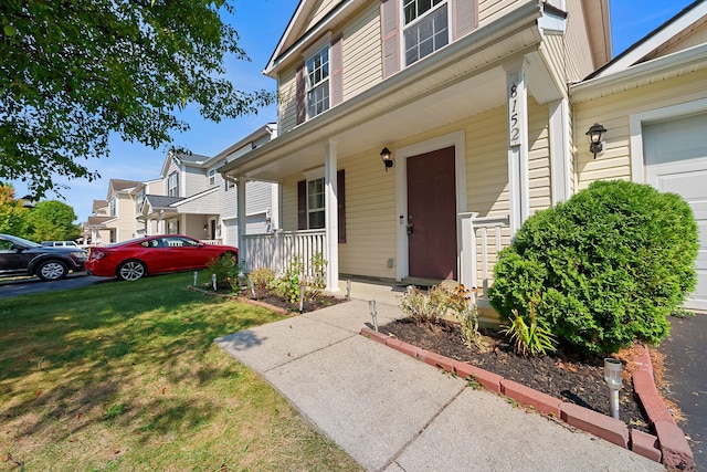 doorway to property featuring covered porch, a lawn, a residential view, and a garage