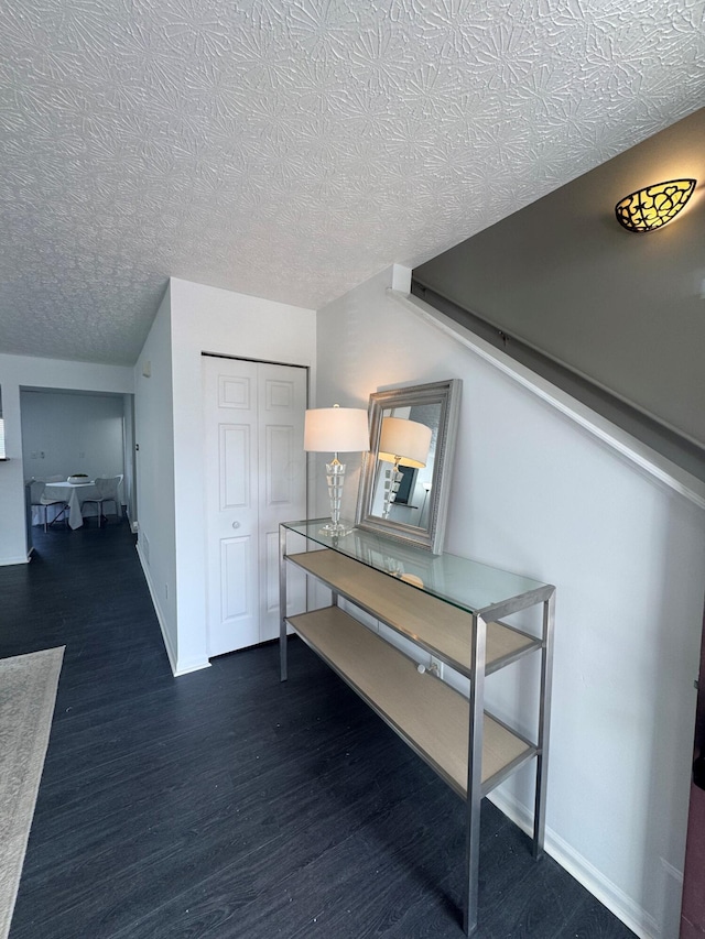 hallway featuring a textured ceiling, wood finished floors, and baseboards