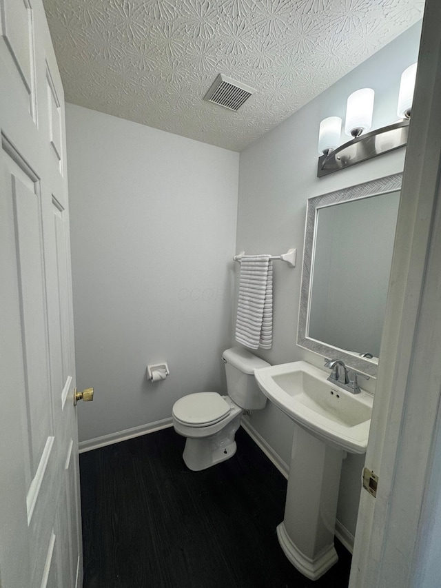 half bathroom featuring baseboards, visible vents, toilet, wood finished floors, and a textured ceiling