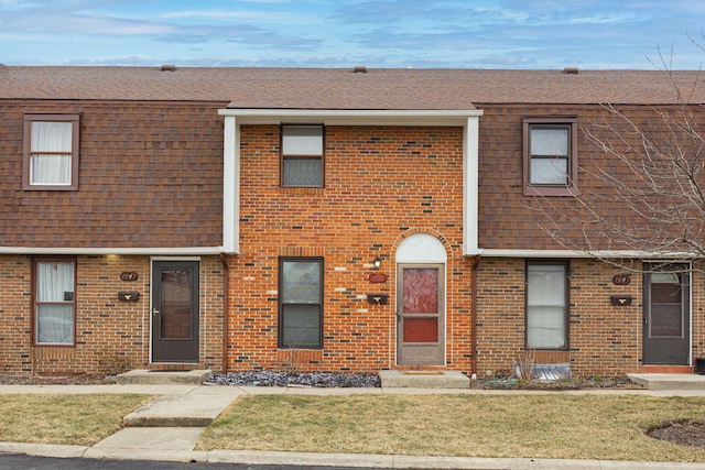 view of property featuring brick siding, roof with shingles, and a front lawn