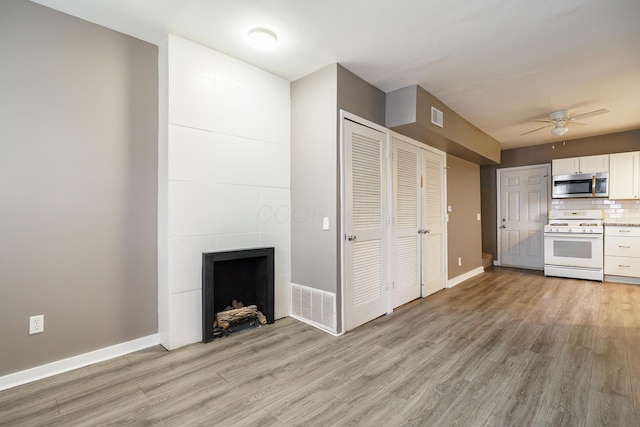 unfurnished living room featuring a tile fireplace, visible vents, a ceiling fan, baseboards, and light wood-type flooring