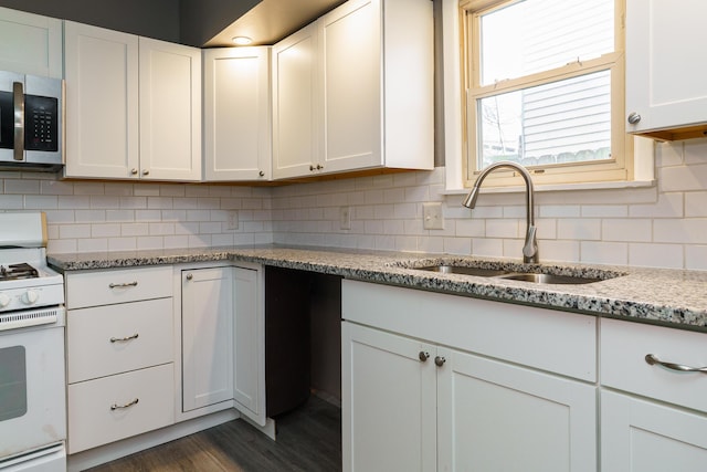 kitchen featuring stainless steel microwave, backsplash, white cabinets, a sink, and white range with gas stovetop