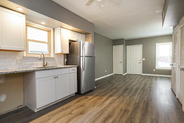 kitchen with dark wood-style floors, tasteful backsplash, freestanding refrigerator, white cabinets, and a sink