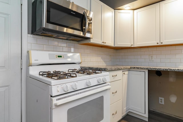 kitchen featuring white gas stove, stainless steel microwave, white cabinets, and decorative backsplash