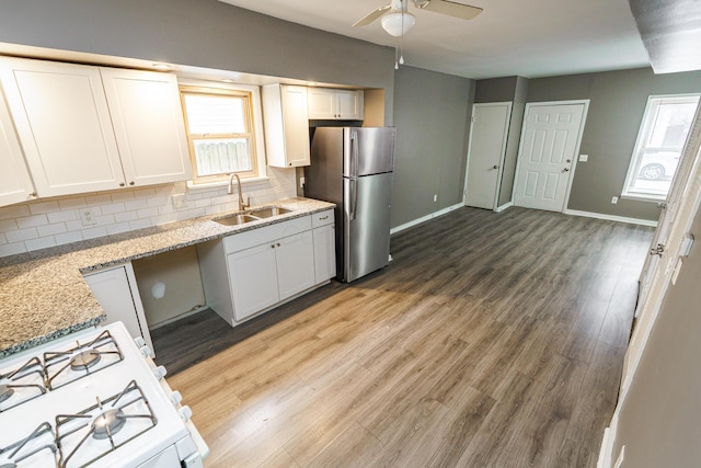 kitchen with a sink, white cabinets, white range with gas cooktop, freestanding refrigerator, and decorative backsplash