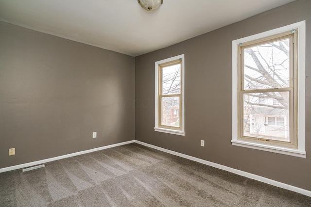 carpeted empty room featuring visible vents, baseboards, and a wealth of natural light