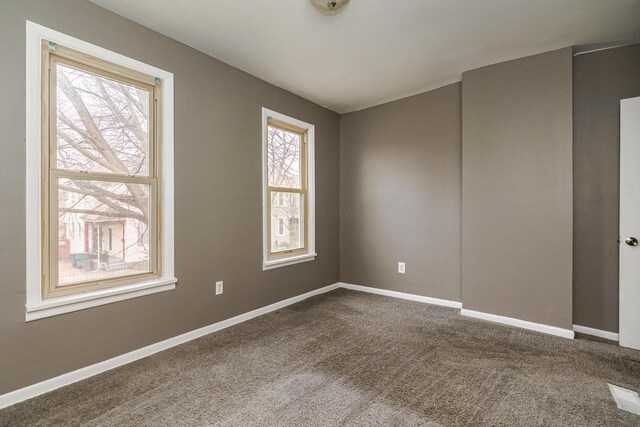 empty room featuring dark carpet, visible vents, and baseboards