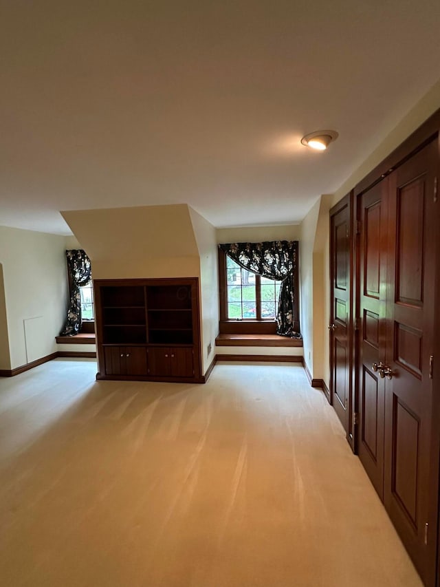 additional living space featuring baseboards and light colored carpet