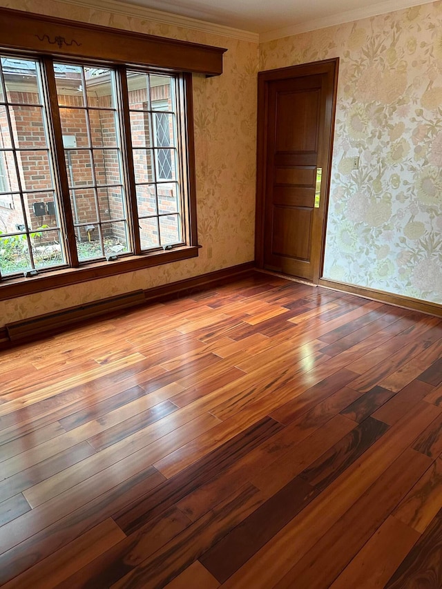 empty room featuring wallpapered walls, crown molding, baseboards, and hardwood / wood-style floors