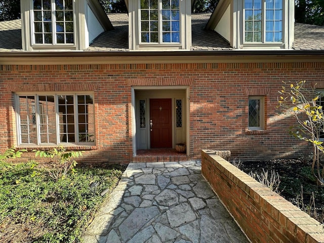 property entrance featuring a shingled roof and brick siding