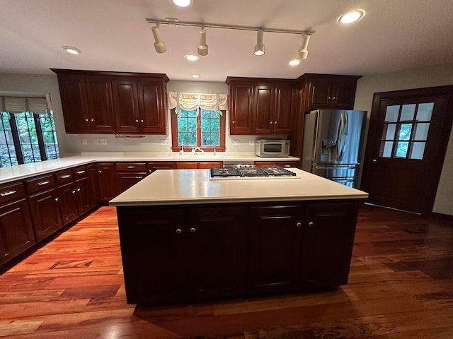 kitchen featuring stainless steel refrigerator with ice dispenser, light countertops, white microwave, gas cooktop, and wood finished floors