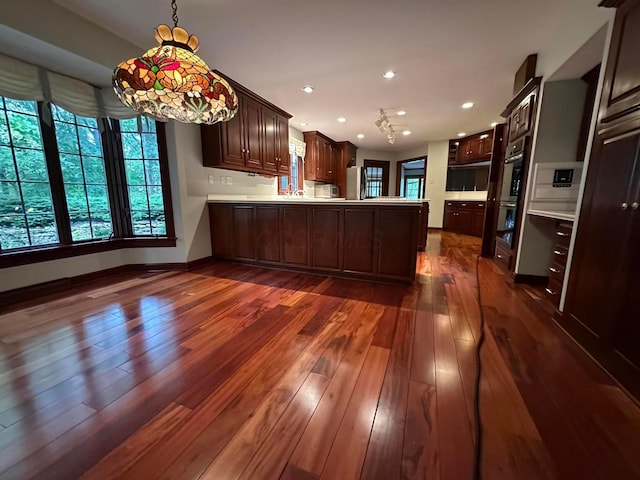 kitchen with refrigerator, a peninsula, light countertops, dark brown cabinets, and dark wood finished floors