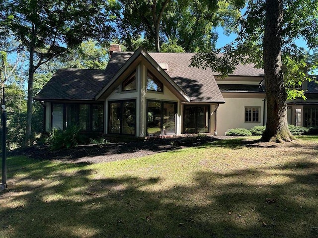 rear view of house featuring a yard, a chimney, a sunroom, and stucco siding