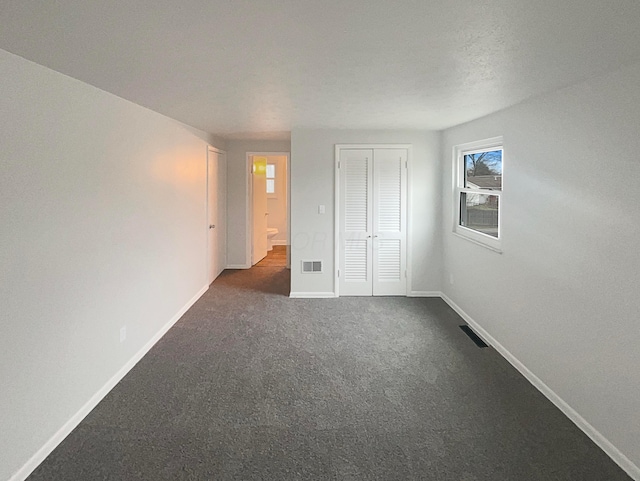 unfurnished bedroom featuring a closet, dark carpet, visible vents, and baseboards