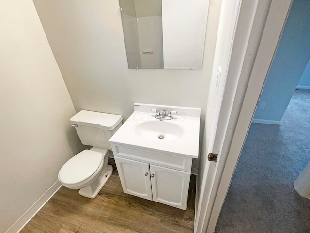 half bathroom featuring toilet, baseboards, wood finished floors, and vanity