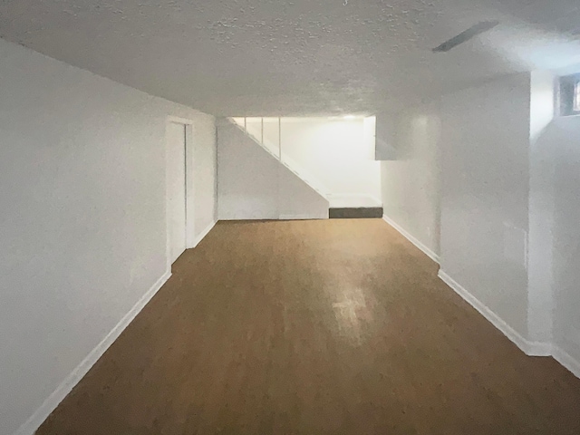 finished below grade area featuring baseboards, a textured ceiling, and wood finished floors