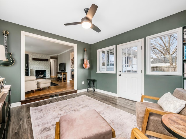 living room featuring a brick fireplace, baseboards, dark wood-style floors, and ceiling fan