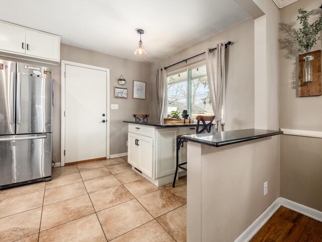 kitchen featuring light tile patterned floors, baseboards, freestanding refrigerator, a peninsula, and white cabinetry