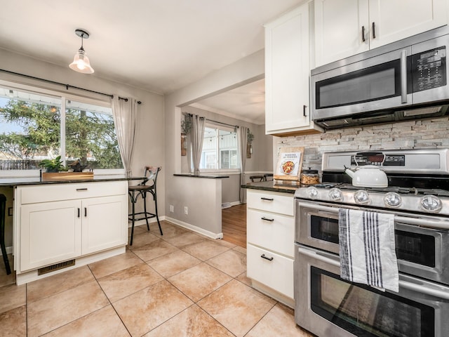 kitchen featuring light tile patterned flooring, white cabinets, appliances with stainless steel finishes, tasteful backsplash, and dark countertops