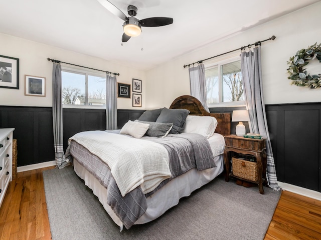 bedroom with a wainscoted wall, ceiling fan, and wood finished floors